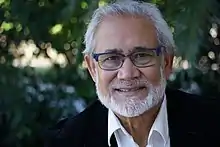 A head and shoulders portrait of a fifty-something man with white hair and glasses, looking into the camera