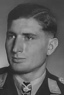 The head of a young man, shown in semi-profile. He wears a military uniform with a military decoration displayed at the front of his shirt collar.