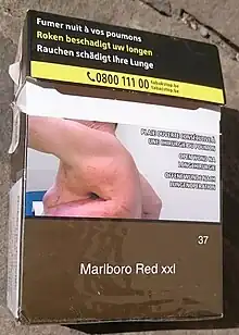 A cigarette package features warning text and a large photograph of a person with a large side wound.