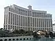 Ground-level view of a broad, 40-story building; the structure is curved, and has a tan facade. A body of water is visible in the foreground.