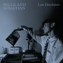 A blue-tinted picture of a man holding a photograph he is developing in a darkroom, with the artist name and title printed above him.