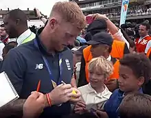 Photograph showing Stokes in a crowd, facing right, signing a ball.