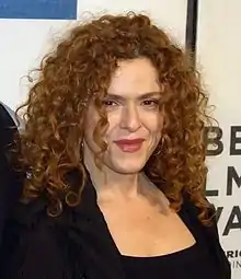 Middle-aged woman with long, curly hair wearing a black sleeveless dress.