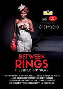 Against a dark background, Esther Phiri stands facing the camera. She is wearing a white formal strapless dress, a white hat with lace decoration, and a pearl necklace - reminiscent of bridal wear, and on her right hand is a red boxing glove.