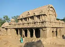 Exterior of a large stone temple, with a man and woman next to it for scale