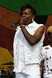 A Black non-binary rapper dressed all in white holds a microphone.