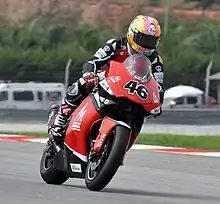 Rider wearing a leather suit and helmet on a red and black racing motorcycle entering a left turn