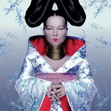 A picture of the album cover depicting a silver background with Björk standing facing forward in the middle. Björk is dressed in an outfit resembling a Kimono wearing large rings around her neck, silver fingernails and a large bun shaped hair style on each side of her head.