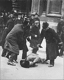 A suffragette lying on the ground, holding her face, while a policeman stands above her