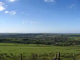 small village in a valley surrounded by green fields with the sea visible in the background