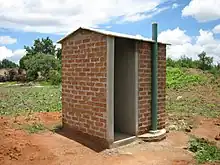 A small brick structure with four walls, an empty doorway, and a tall exhaust pipe.