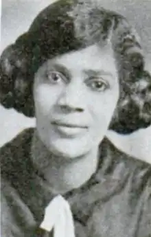 A young Black woman with hair in two side buns, wearing a dark blouse with a white bow