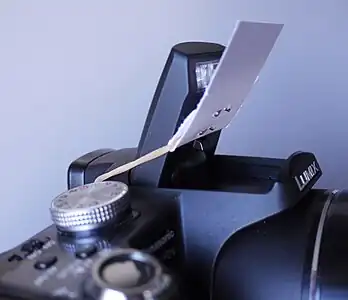 Diffuser on a camera flash. Made from a sheet of paper, a rubber band, and two staples.