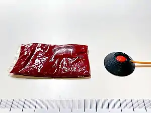 A 15 ml packet of fake blood next to a 0.5 grain squib with a solid polycarbonate backing/shield.