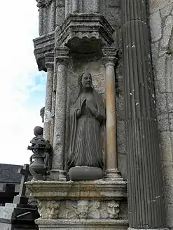 The kneeling Virgin Mary looks across to Gabriel. This sculpture is by Roland Doré. Around the vase containing lilies, is a banner reading "ECCE:ANCILLA:D(OMI)NI:FIAT:MIHI: SECVNDVM:VERBVM:TVVM"