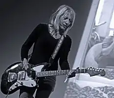 A woman plays a guitar in front of a projection screen.