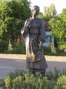 A bronze-colored statue of a standing woman in a plain dress