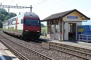 Double-decker train passes small enclosed waiting area