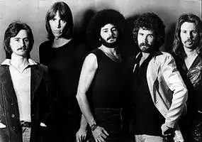 1976 black-and-white photo of the American rock band Boston for their self-titled debut studio album Boston. From left to right guitarist Barry Goudreau, founder, leader, and multi-instrumentalist Tom Scholz, drummer Sib Hashian, singer Brad Delp, and bassist Fran Sheehan.