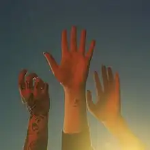 Three hands in front of a pale blue sky, light shining from the bottom right corner