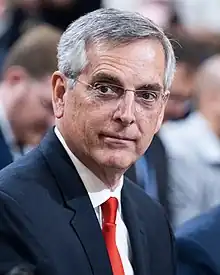 Brad Raffensperger wearing a grey suit with a name tag.