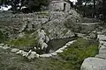 The pool of the sacred spring with the stepped retaining wall (left), the temple podium and the church of Hagios Georgios at center