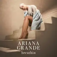 Cover art for "Breathin": Ariana Grande with a white wig and a denim jacket, tilting her head and sitting on a brown staircase