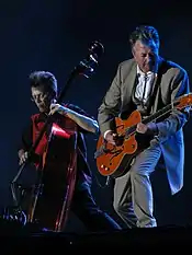 Brian Setzer, in a gray suit, strumming a guitar