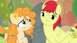 A female orange pony and a male yellow pony stand in front of a carved rock, looking at each other lovingly.