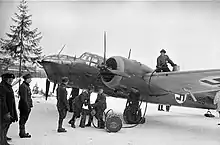 A Finnish bomber plane is being refueled by hand by six servicemen at an air base on a frozen lake.