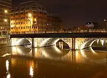 A three-arched bridge viewed from an oblique angle, illuminated by lights