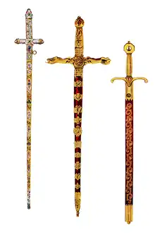 Three swords: one of gold and silver appearance covered in stones, the others red with gilded handles and decorations