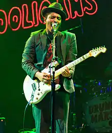 Mars, in a black suit and hat, playing guitar onstage