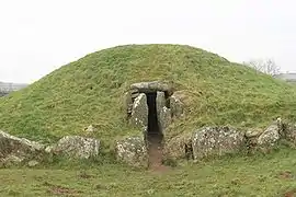 A low grassy mound with an entrance at its centre framed by cyclopean stones