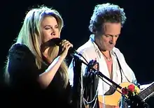 A blonde, female singer and a male acoustic guitarist are performing together in concert.