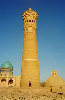 A tall minaret, with domed structures and a blue sky behind.