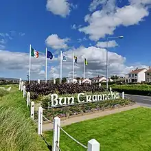 A large sign which reads Bun Cranncha (Buncrana in Irish) which is surrounded by a number of flags. This can be seen when entering the town via Railway Road R238