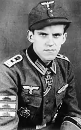 A man wearing a military uniform, side cap, various military decorations including an Iron Cross displayed at the front of his uniform collar.