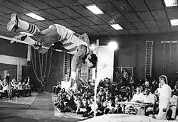 Rolf Beilschmidt jumps over a bar while spectators look on