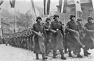 a black and white photograph of soldiers in German uniform and greatcoats marching in a column