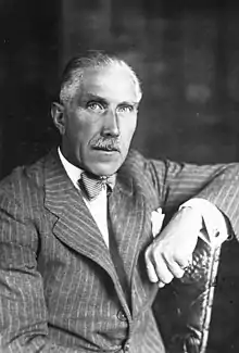 Portrait of an elderly man with grey hair and moustache in a pinstripe suit.