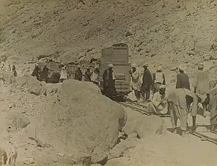 A crowd of workers pushing rail cars along tracks while others lay more tracks in front