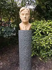 Outdoor bust of middle aged man with good head of hair, against a garden background