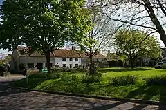 Grassy area with trees in the foreground and a terrace of stone houses, one white fronted, in the background