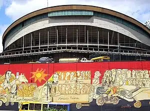 A bright red and orange mural in the lower half, a concrete stadium above it.