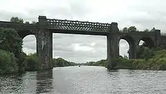 Wide river sized canal with high metal bridge supported on Masonry pillars having arches on either side