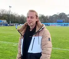 Man in a warm coat standing on a football pitch looking in front of him