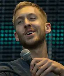 Calvin Harris performing in a blue shirt with green lights behind him.