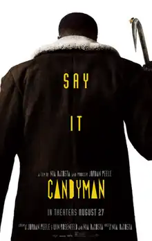 The Candyman faces opposite the viewer. On top of his large dark coat are the words "Say It" and "Candyman" in yellow font.
