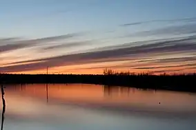 An orange sunset reflects in a quiet and calm Cane Creek Lake with a timber line on the horizon